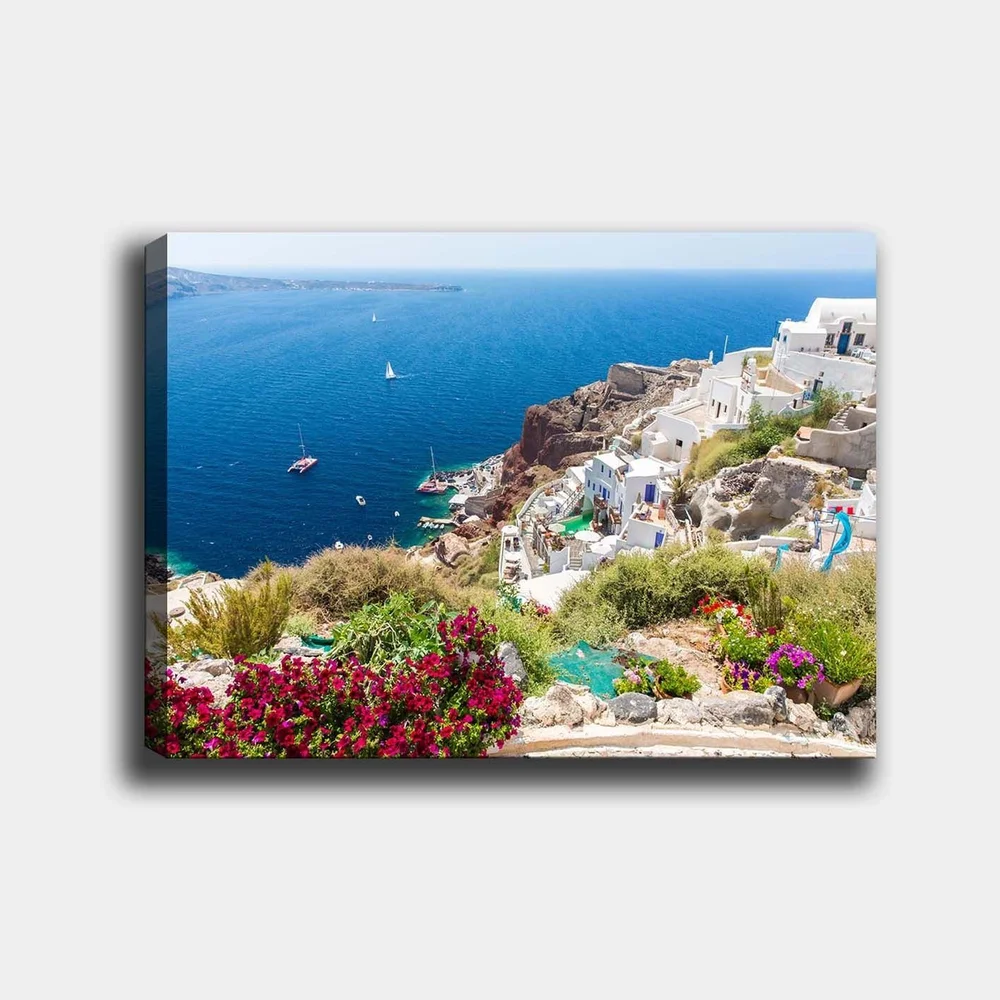 Lerretsbilde 70x100 cm - Vakker utsikt over Santorini med hvite hus og blomster som pryder klippene ved havet v:7108070